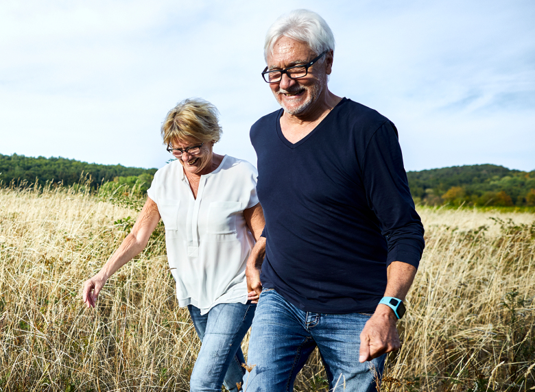 An elderly couple holding hands and walking through a grassy field