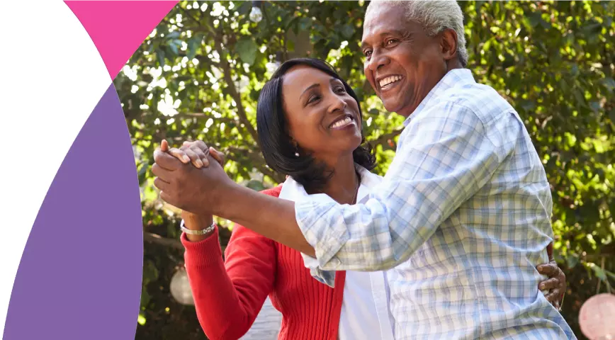 An elderly couple dancing together outside while smiling